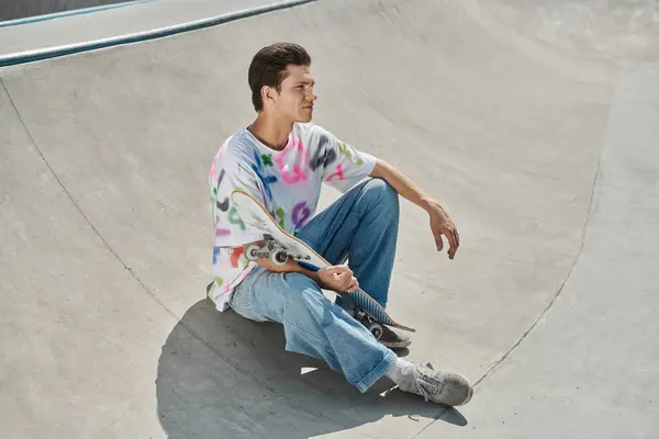 A young skater boy showcases his skills, sitting on a skateboard in a vibrant skate park. — Stock Photo