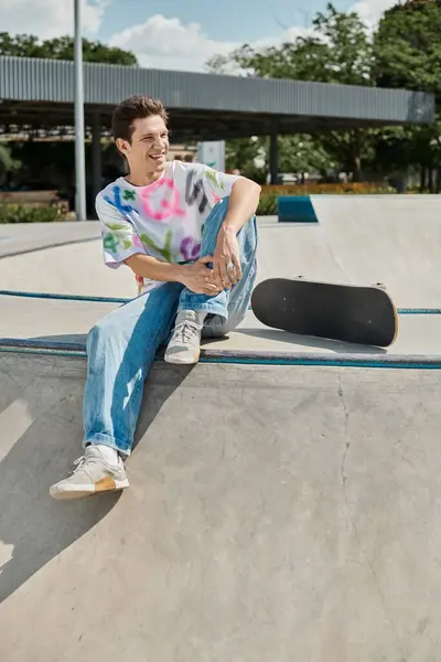 A young man sits pensively on the edge of a skateboard ramp, soaking in the thrill of the impending descent at a skate park. — Stock Photo
