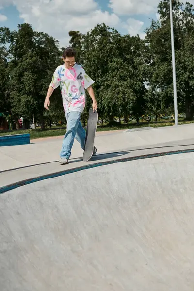Un joven patinador caminando con monopatín por una empinada rampa en un parque de skate en un soleado día de verano. - foto de stock