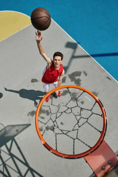 Un joven vibrante con una camisa roja gotea una pelota de baloncesto con concentración y determinación en un día soleado. - foto de stock