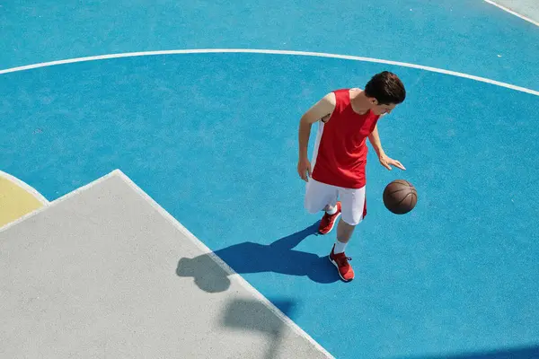 Un joven se para en una cancha de baloncesto sosteniendo una pelota, preparándose para jugar en un día soleado. - foto de stock