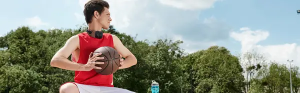 Ein junger Mann in einem leuchtend roten Hemd spielt an einem sonnigen Sommertag im Freien Basketball. — Stockfoto