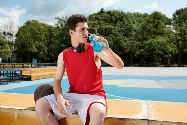 Un joven se sienta en una repisa bebiendo de una botella de agua en un día soleado. - foto de stock