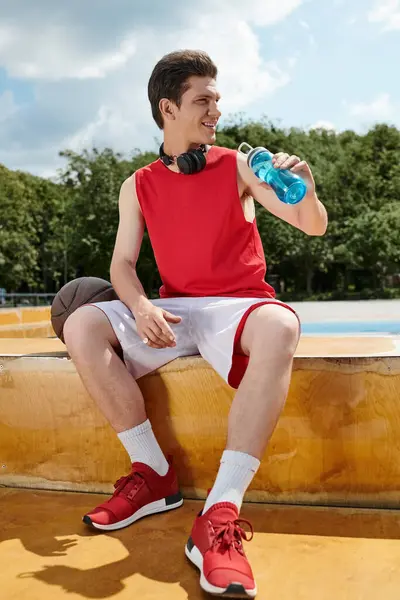 Un uomo seduto su un cornicione, che si prende una pausa per idratarsi con una bottiglia d'acqua in mano. — Foto stock