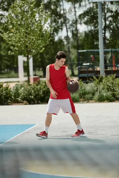 Un joven se para en una cancha de baloncesto, sosteniendo una pelota en su mano, listo para jugar bajo el sol de verano. - foto de stock