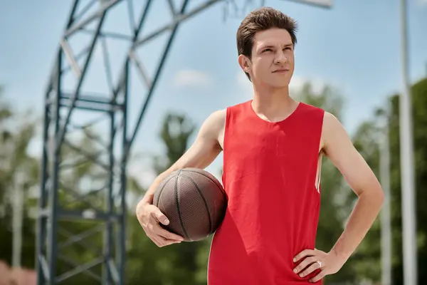 Um jovem com uma camisa vermelha vibrante habilmente mantém uma bola de basquete enquanto joga ao ar livre em um dia de verão. — Fotografia de Stock