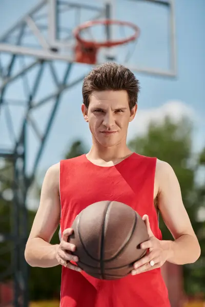 A young man in a red shirt skillfully dribbles a basketball outside on a sunny summer day. — Stock Photo