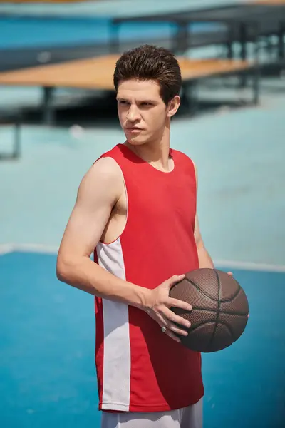 Um jogador de basquete jovem em um campo, habilmente segurando sua bola em um dia ensolarado de verão. — Fotografia de Stock