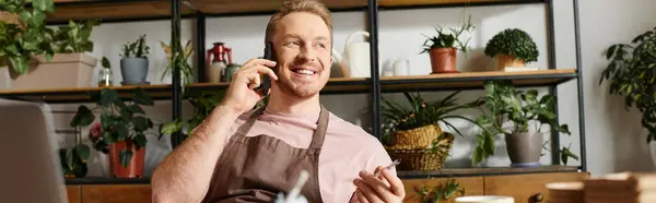 Um homem focado senta-se em uma mesa em uma loja da planta, acoplando-se em uma chamada telefônica ao controlar seu negócio pequeno. — Fotografia de Stock