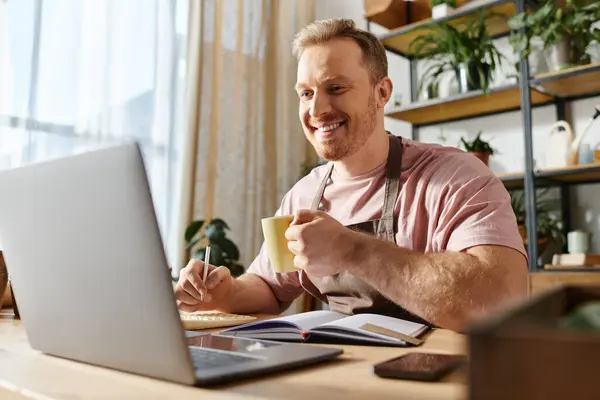 Um homem bonito senta-se na frente de um computador portátil, cercado por plantas em sua loja de plantas, incorporando o conceito de possuir um pequeno negócio. — Fotografia de Stock
