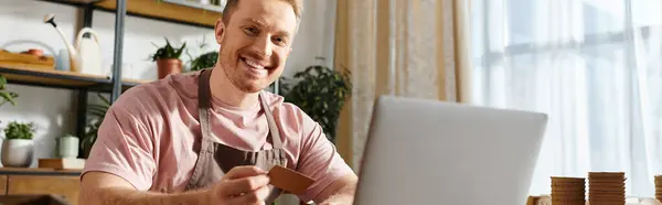 Un hombre se sienta frente a una computadora portátil, trabajando en su pequeño negocio en una tienda de plantas. Concepto de negocio propio. - foto de stock