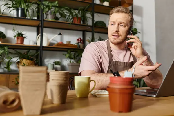 A man sits at a table in a plant shop, engaged in a phone call. The setting exudes a small business owners vibe. — Stock Photo