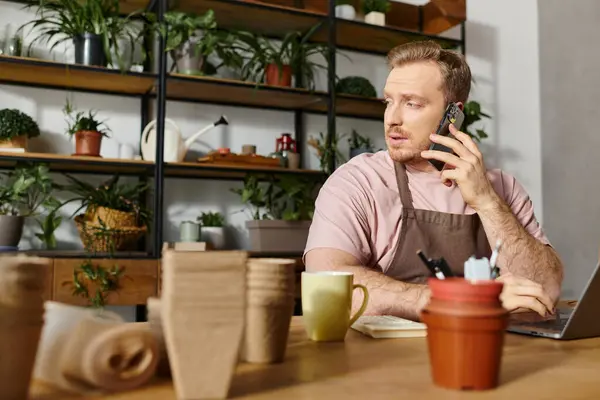 A man sits at a table in a plant shop, engrossed in conversation on his cell phone, embodying a small business owner in action. — Stock Photo