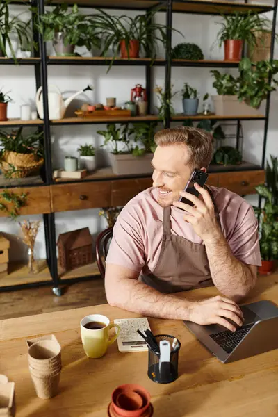 A man sitting at a table talking on a cell phone in a plant shop, embodying the concept of owning a small business. — Stock Photo