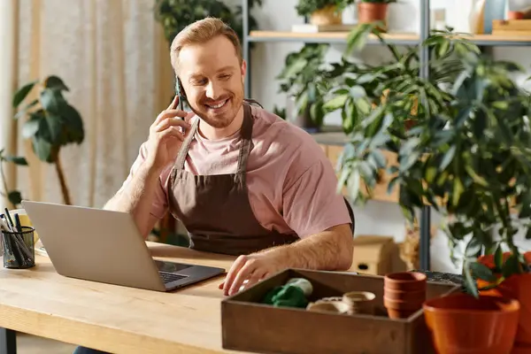 A man, owning a plant shop, conducts business on a cell phone at his desk with determination. — Stock Photo