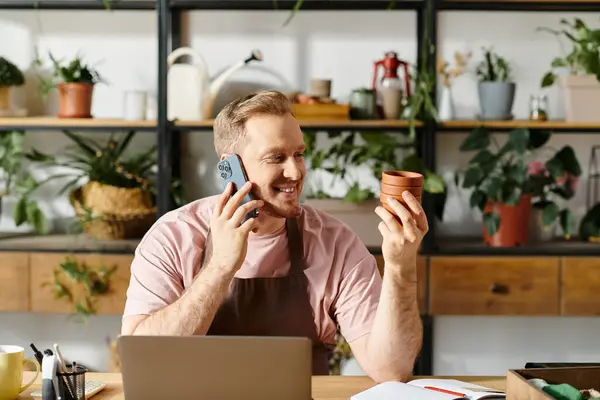 Un hombre sentado en una mesa en una tienda de plantas, conversando en un teléfono celular, exudando un sentido de enfoque y profesionalismo. - foto de stock