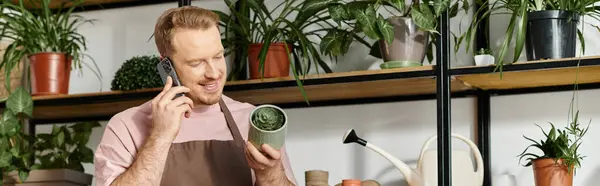 Un uomo soave multitasking con un cellulare in mano e un vaso di piante tenuto senza sforzo, mostrando il suo spirito imprenditoriale in un negozio di piante. — Foto stock
