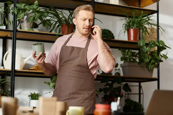 A man in an apron multitasks, taking a call while managing his plant shop business. — Stock Photo