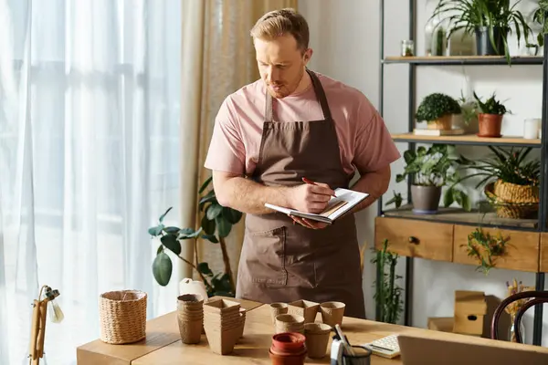 Ein Mann in Schürze macht sich in einem Pflanzenladen fleißig Notizen auf einem Klemmbrett und zeigt sein Engagement für sein kleines Geschäft. — Stockfoto