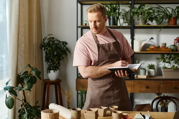 A man stands confidently in front of a wooden table in his plant shop, embodying the essence of his small business. — Stock Photo