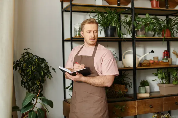A charismatic man in an apron confidently holds a clipboard in a plant shop, embodying the spirit of entrepreneurship and organization. — Stock Photo