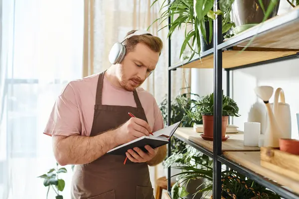 A man in an apron and headphones takes notes on a clipboard in a vibrant plant shop, embodying a dedicated small business owner. — Stock Photo