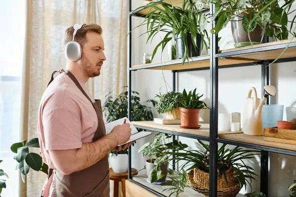 A man in headphones surrounded by lush green plants in a small shop. — Stock Photo