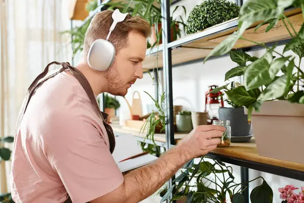 A man with headphones gazes at a plant in a plant shop, embodying the essence of nature and music in perfect harmony. — Stock Photo