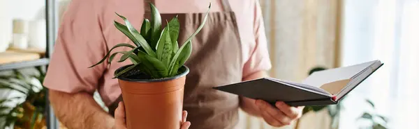 A cropped man holding a potted plant and a notebook. — Stock Photo
