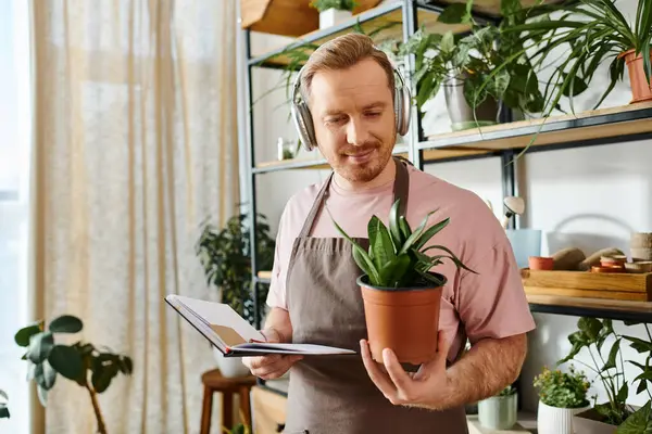 Um homem em um avental carinhosamente detém uma planta em vaso, mostrando sua paixão por plantas e natureza. — Fotografia de Stock