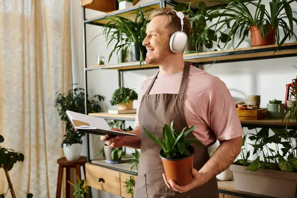 A man in an apron holding a potted plant in a plant shop, showcasing his passion for gardening. — Stock Photo
