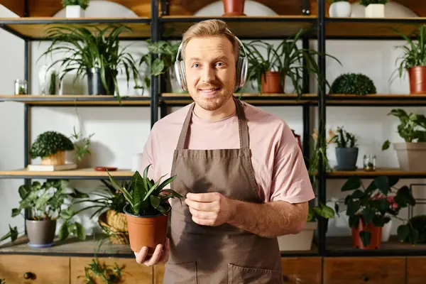 A man in an apron carefully holds a potted plant, showcasing his dedication to his small florist business. — Stock Photo
