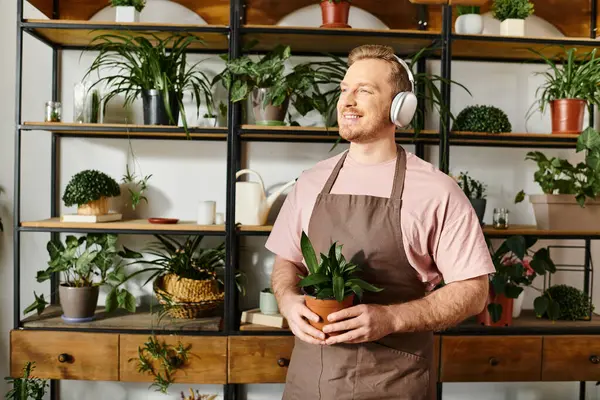 Um homem com fones de ouvido equilibrando uma planta em vaso, imerso em música e cuidando de sua vegetação. — Fotografia de Stock