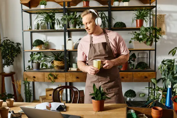 A man in an apron enjoying a cup of coffee in a plant shop, showcasing the concept of owning a small business. — Stock Photo