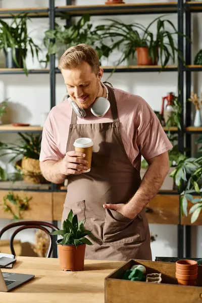 A handsome man in an apron enjoying a cup of coffee in his plant shop, embodying the idea of owning a small business. - foto de stock