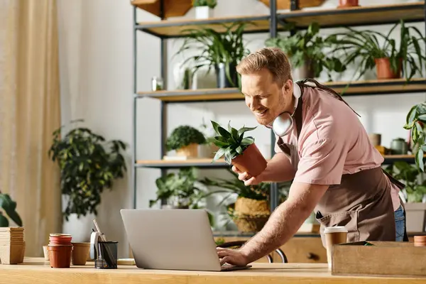 Um homem de camisa rosa se concentra intensamente em seu laptop enquanto trabalha em sua loja de plantas, incorporando a essência de um pequeno empresário.. — Fotografia de Stock