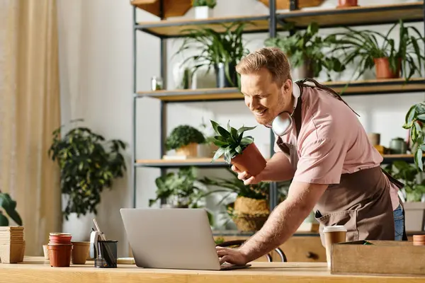 A man in a pink shirt focuses intently on his laptop while working in his plant shop, embodying the essence of a small business owner. — Stock Photo