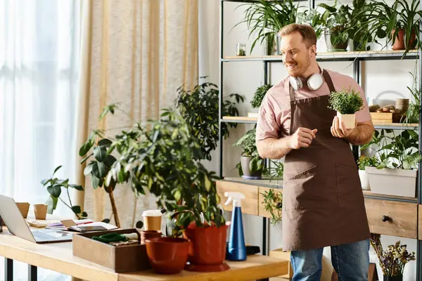 Un bell'uomo in grembiule tiene orgogliosamente una pianta in vaso in un negozio di piante, mostrando il suo amore per il verde.. — Foto stock