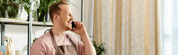 Un hombre en una habitación, involucrado en una conversación telefónica mientras dirigía su pequeño negocio, una tienda de plantas. - foto de stock