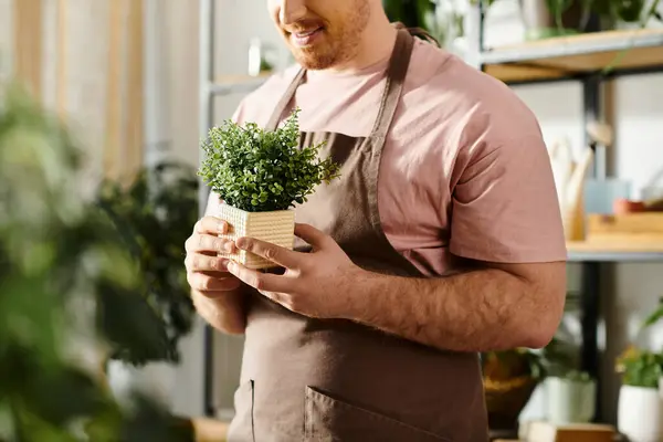 Um homem em um avental prende uma planta potted, mostrando seu amor para nutrir a vida verde em sua loja da planta. — Fotografia de Stock