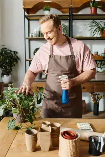 Um homem com um avental segura uma garrafa de spray em uma loja de plantas, mostrando sua experiência em nutrir vegetação para sua pequena empresa. — Fotografia de Stock