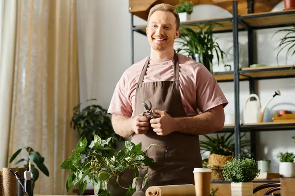 Un hombre guapo está en su tienda de plantas, rodeado de vegetación y varias plantas en maceta en una mesa. - foto de stock