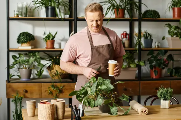 A charismatic man in an apron enjoys a cup of coffee in his plant shop, embodying the essence of entrepreneurship. — Stock Photo