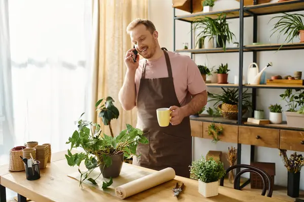 Man stands in kitchen, talking on cell phone, multitasking in small business environment. — Stock Photo