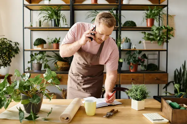 A man in an apron multitasks by talking on his cell phone while managing his plant shop business. — Stock Photo