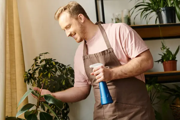 A man in an apron holding a spray bottle, tending to plants in a small business plant shop. — Stock Photo