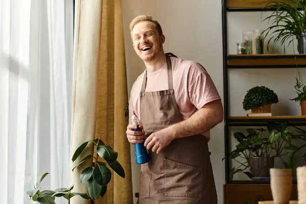 Un hombre carismático con un delantal sosteniendo una botella de spray azul en una encantadora tienda de plantas. - foto de stock