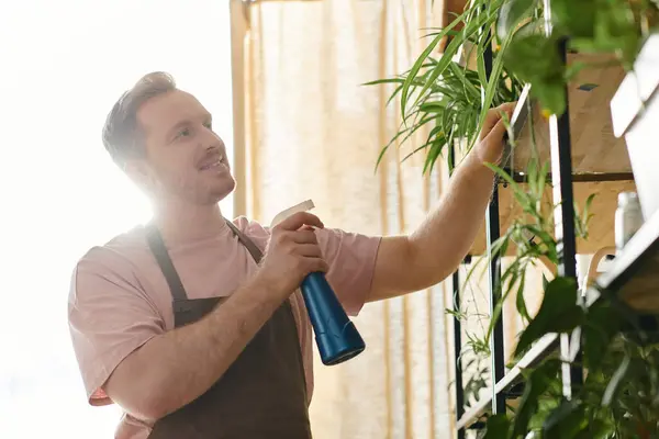 Чоловік тримає пляшку синього розпилювача перед яскравою рослиною, збільшуючи її зростання в сюрреалістичній садовій обстановці. — стокове фото