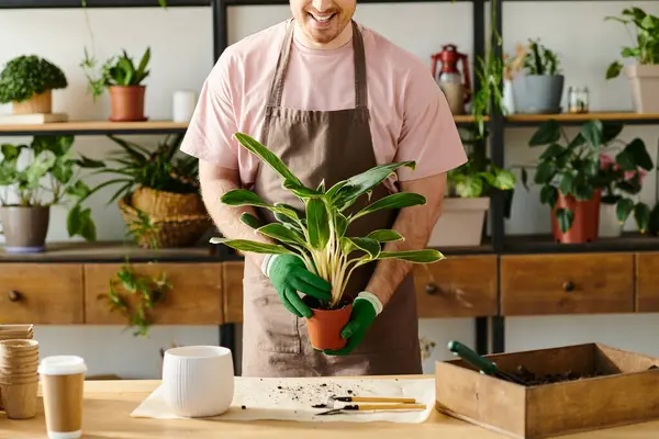 A man delicately holds a potted plant on a wooden table in a quaint plant shop, showcasing his love for greenery. - foto de stock