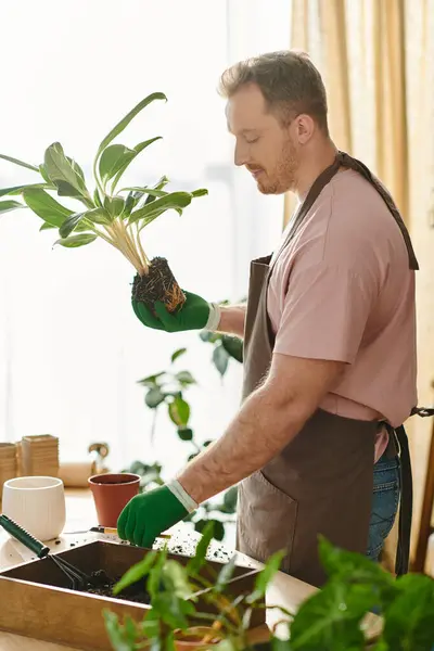 Um homem bonito com uma planta envasada em suas mãos, mostrando sua paixão por plantas e natureza em sua pequena florista. — Fotografia de Stock